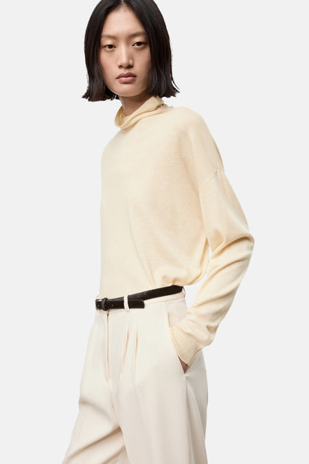 Ecru coltrui van MANGO, gedragen met een broek met hoge taille en een bruine riem, van achteren gezien.