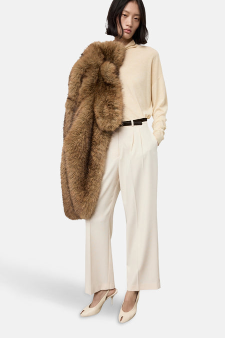 Pull à col roulé écru de MANGO, porté avec un manteau en fourrure marron, un pantalon taille haute et des escarpins en cuir.