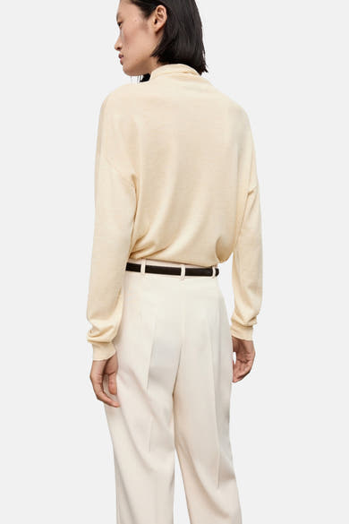 Pull à col roulé écru de MANGO, porté avec un pantalon taille haute et une ceinture marron, vue de dos.
