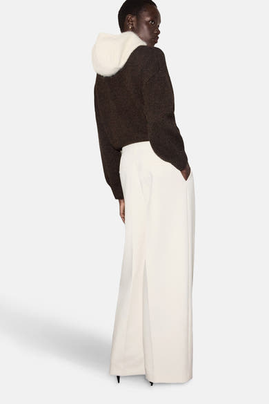 Pull à col rond brun par MANGO, avec capuche contrastante blanche, porté avec un pantalon blanc large.