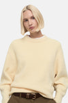 Pull à col rond jaune de MANGO, porté avec un pantalon marron et une ceinture en cuir.