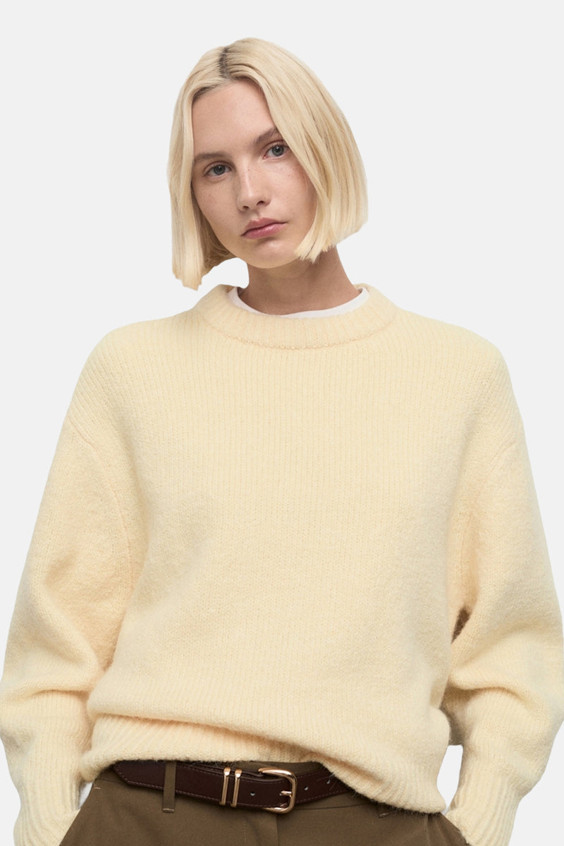 Pull à col rond jaune de MANGO, porté avec un pantalon marron et une ceinture en cuir.