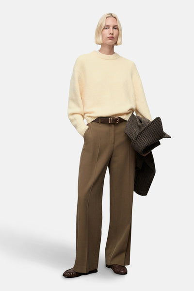 Pull à col rond jaune de MANGO, porté avec un pantalon marron taille haute et une ceinture en cuir.
