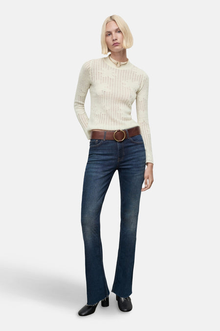 Pull à col rond beige de MANGO avec un motif ajouré, porté avec un jean bleu et une ceinture marron.
