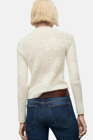 Pull à col rond beige, par MANGO, à maille ajourée porté avec un jean et une ceinture marron.