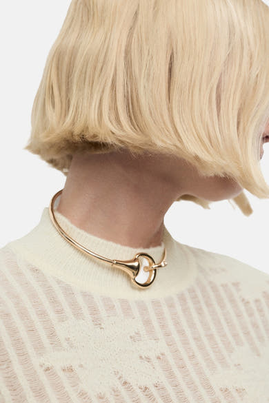 Pull à col rond beige de MANGO, porté avec un collier ras de cou doré et une coiffure blonde courte.