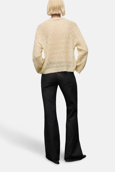 Pull à col rond beige de MANGO, à motif texturé ajouré, porté avec un pantalon noir évasé, vue de dos.