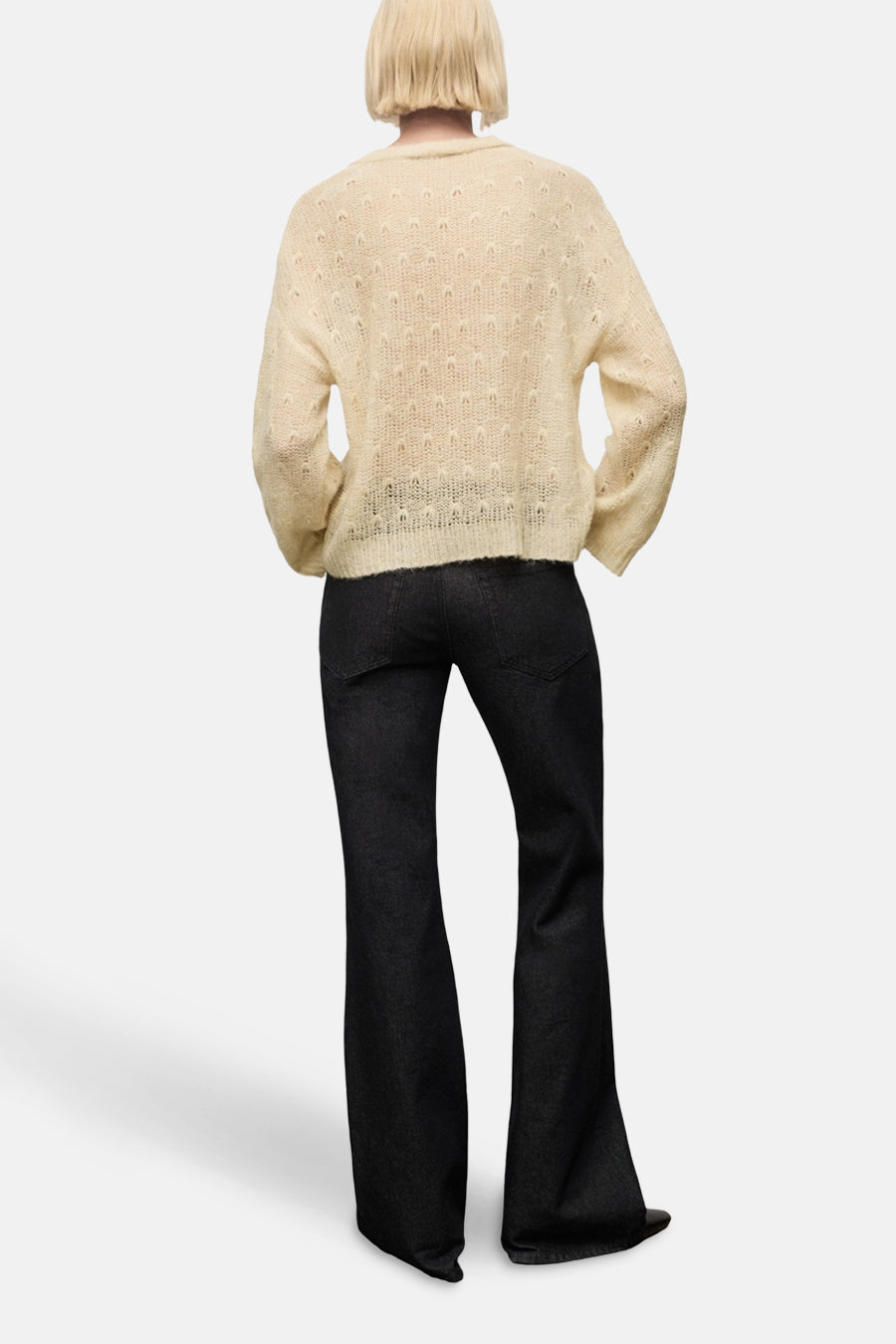 Pull à col rond beige de MANGO, à motif texturé ajouré, porté avec un pantalon noir évasé, vue de dos.