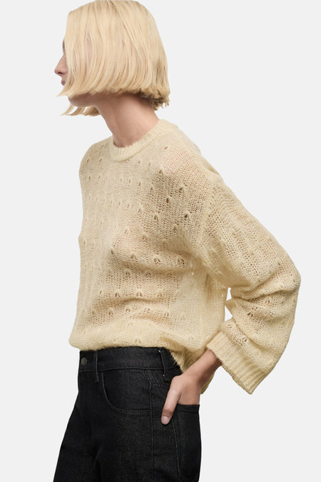 Beige ronde hals trui van MANGO, in ajour gebreid, gedragen met een zwarte high-waist broek.