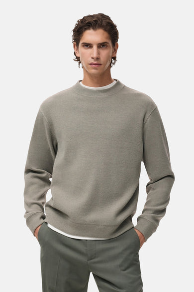 Sweat gris col rond de MANGO, avec une texture fine et porté sur un t-shirt blanc et un pantalon olive.
