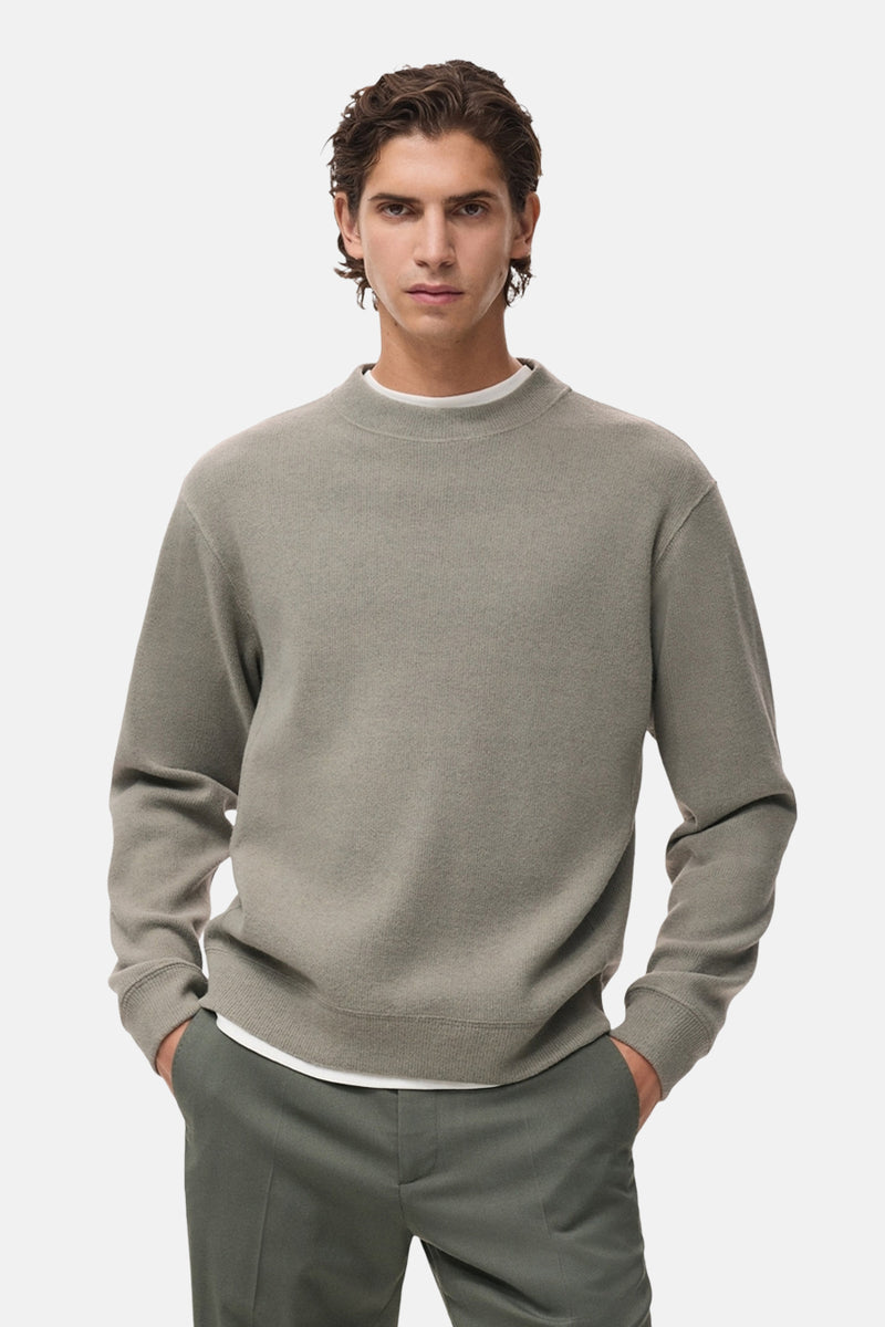 Sweat gris col rond de MANGO, avec une texture fine et porté sur un t-shirt blanc et un pantalon olive.