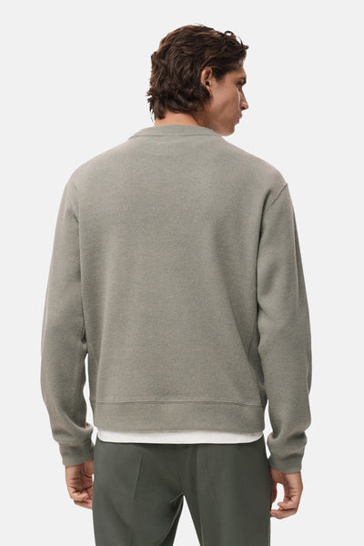 Sweat-shirt gris en maille de MANGO, avec une texture gaufrée, porté sur un t-shirt blanc et un pantalon vert olive.