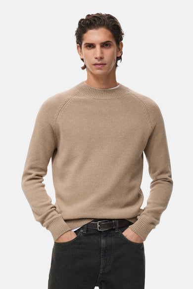 Pull à col rond beige de MANGO, porté avec un jean noir et une ceinture en cuir.