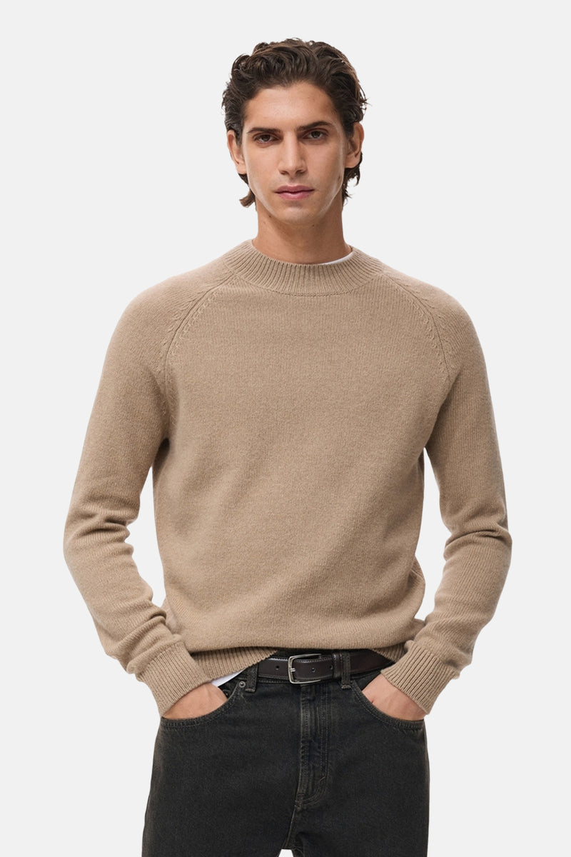 Pull à col rond beige de MANGO, porté avec un jean noir et une ceinture en cuir.