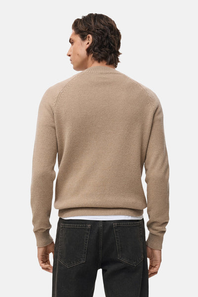 Pull à col rond beige de MANGO, porté avec un jean noir et un t-shirt blanc visible au niveau de la taille.