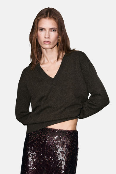 Bruine V-hals trui van MANGO, gedragen met een bordeaux paillettenrok en muiltjes met hak.
