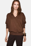 Pull à col en V brun de MANGO, porté avec un pantalon marron et un bracelet texturé.