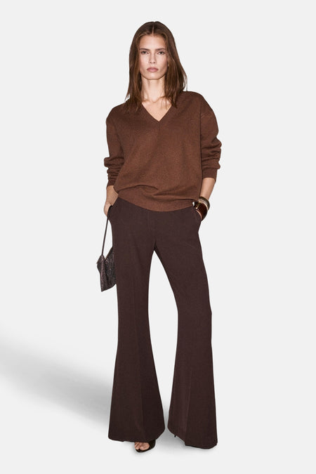 Pull à col en V brun de MANGO, porté avec un pantalon évasé marron et un petit sac à main.
