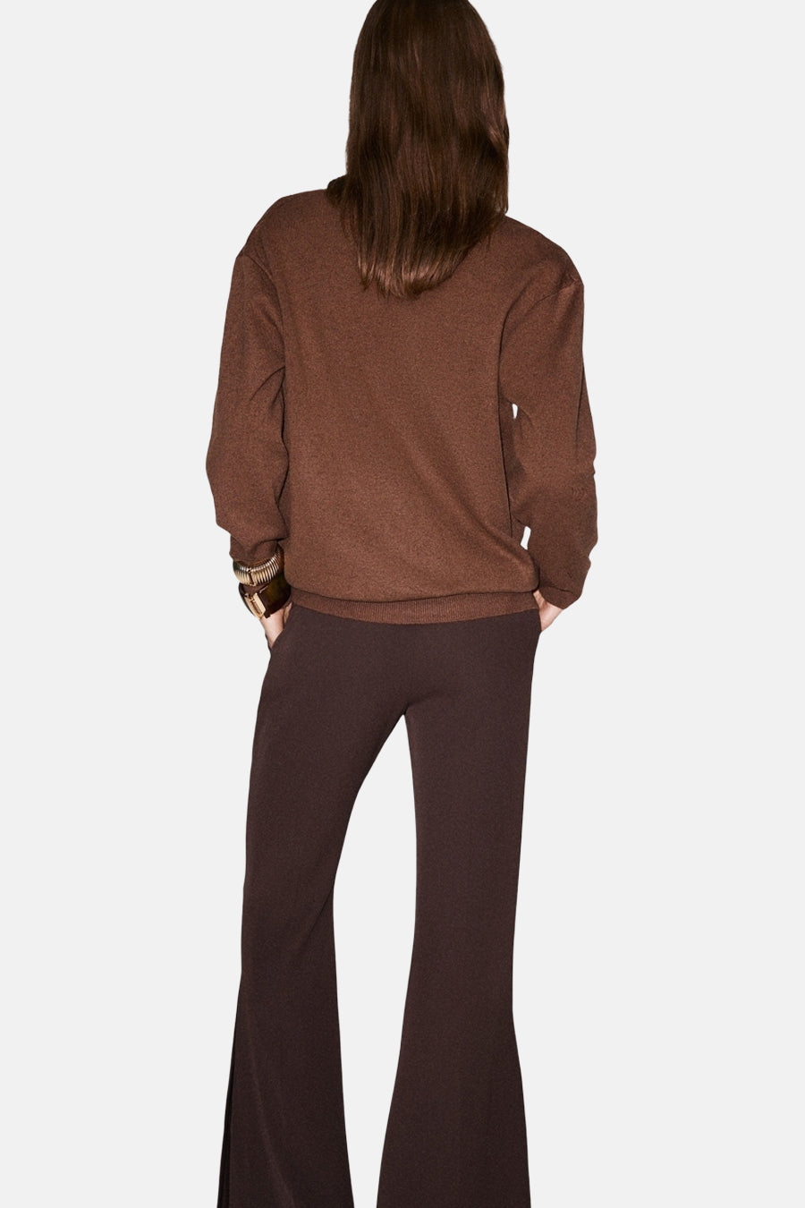 Pull à col en V brun de MANGO, porté avec un pantalon évasé en maille.
