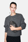 Pull à col rond gris de MANGO, orné de décorations scintillantes sur les épaules, porté avec des boucles d'oreilles pendantes.
