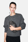 Pull à col rond gris de MANGO avec décorations brillantes sur les épaules, porté avec des boucles d'oreilles pendantes.