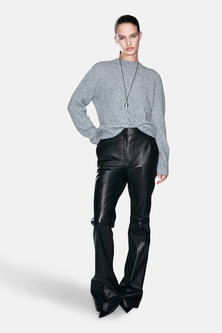 Pull à col rond bleu de MANGO, porté avec un pantalon en cuir noir et un collier avec pendentif.