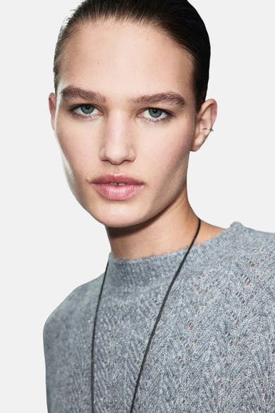 Pull à col rond bleu de MANGO, en tricot texturé porté avec un collier fin.
