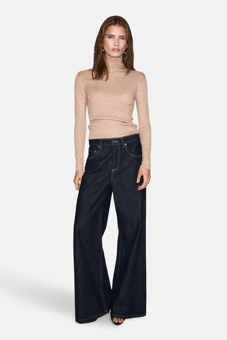 Pull à col roulé beige de MANGO, porté avec un pantalon large en jean brut et des boucles d'oreilles rondes.