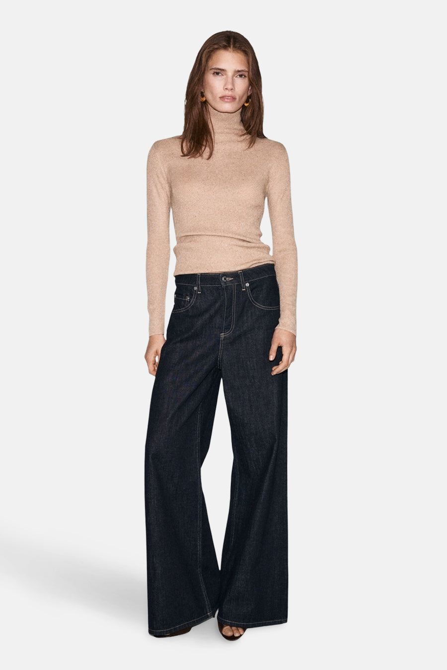Pull à col roulé beige de MANGO, porté avec un pantalon large en jean brut et des boucles d'oreilles rondes.