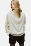 Pull à col roulé écru de MANGO, porté avec un short noir opaque et des collants noirs.