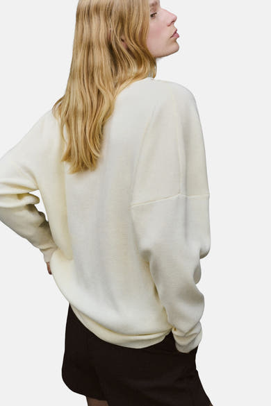 Pull à col roulé écru de MANGO, en maille texturée, porté avec un short noir.