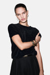 Pull à col rond noir de MANGO, avec des bracelets dorés et une ceinture noire.