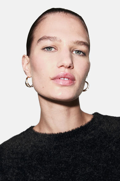 Pull à col rond noir de MANGO, en tricot texturé porté par une femme avec des boucles d'oreilles dorées.
