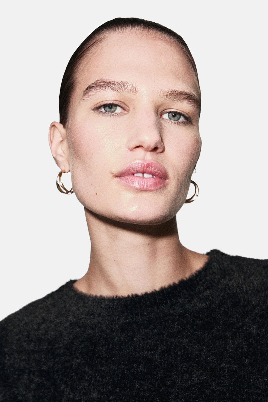 Pull à col rond noir de MANGO, en tricot texturé porté par une femme avec des boucles d'oreilles dorées.
