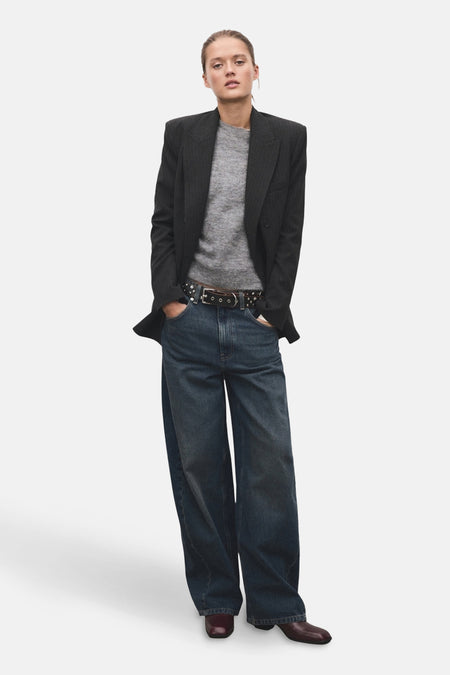 Pull à col rond gris de MANGO, porté avec un blazer anthracite, un jean large et une ceinture cloutée.