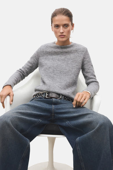 Grijze trui met ronde hals van MANGO, gedragen met een wijde jeans en een leren riem met studs.