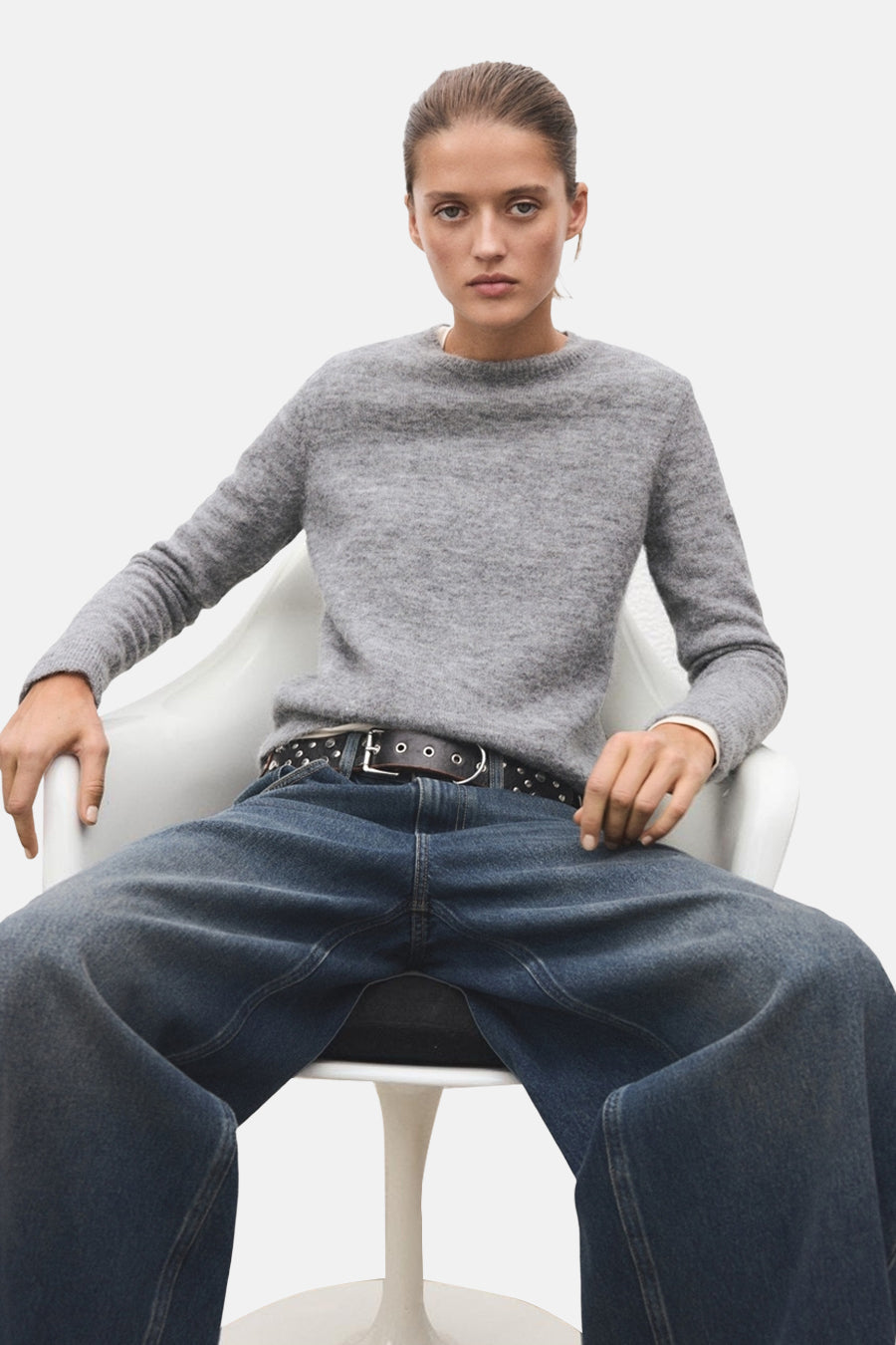 Grijze trui met ronde hals van MANGO, gedragen met een wijde jeans en een leren riem met studs.