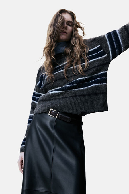Pull à col rond multicolore de MANGO, avec des rayures horizontales et porté avec une jupe en cuir noir.
