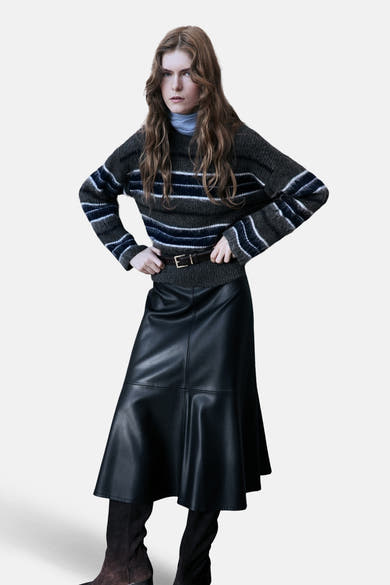 Pull multicolore à col rond de MANGO, porté avec une jupe noire en cuir et des bottes marron.