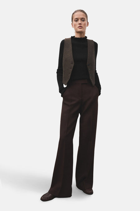 Pull à col rond noir de MANGO, porté avec un gilet marron et un pantalon évasé marron.