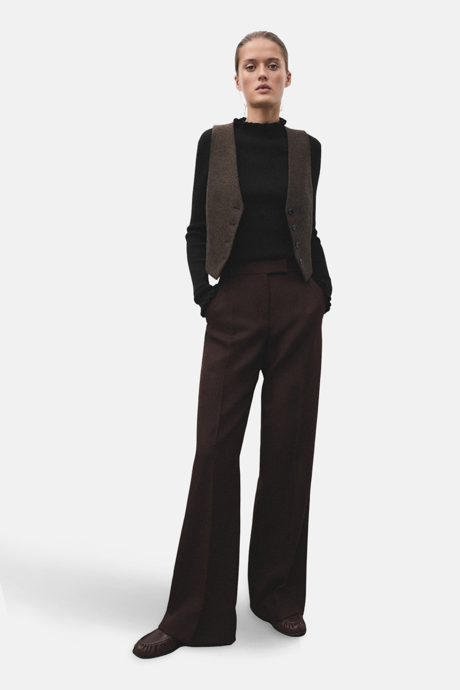 Pull à col rond noir de MANGO, porté avec un gilet marron et un pantalon évasé marron.