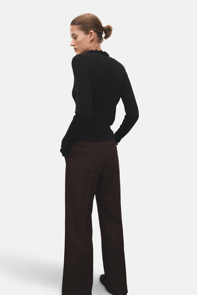 Pull col rond noir de MANGO, en maille côtelée, porté avec un pantalon marron ample, vue de dos.