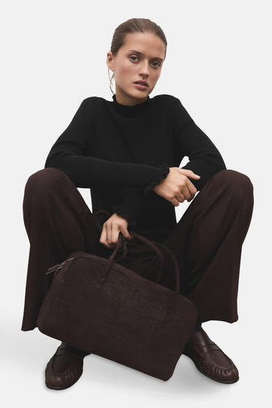 Zwarte rondehals trui van MANGO, gedragen met een wijde bruine broek en leren loafers.