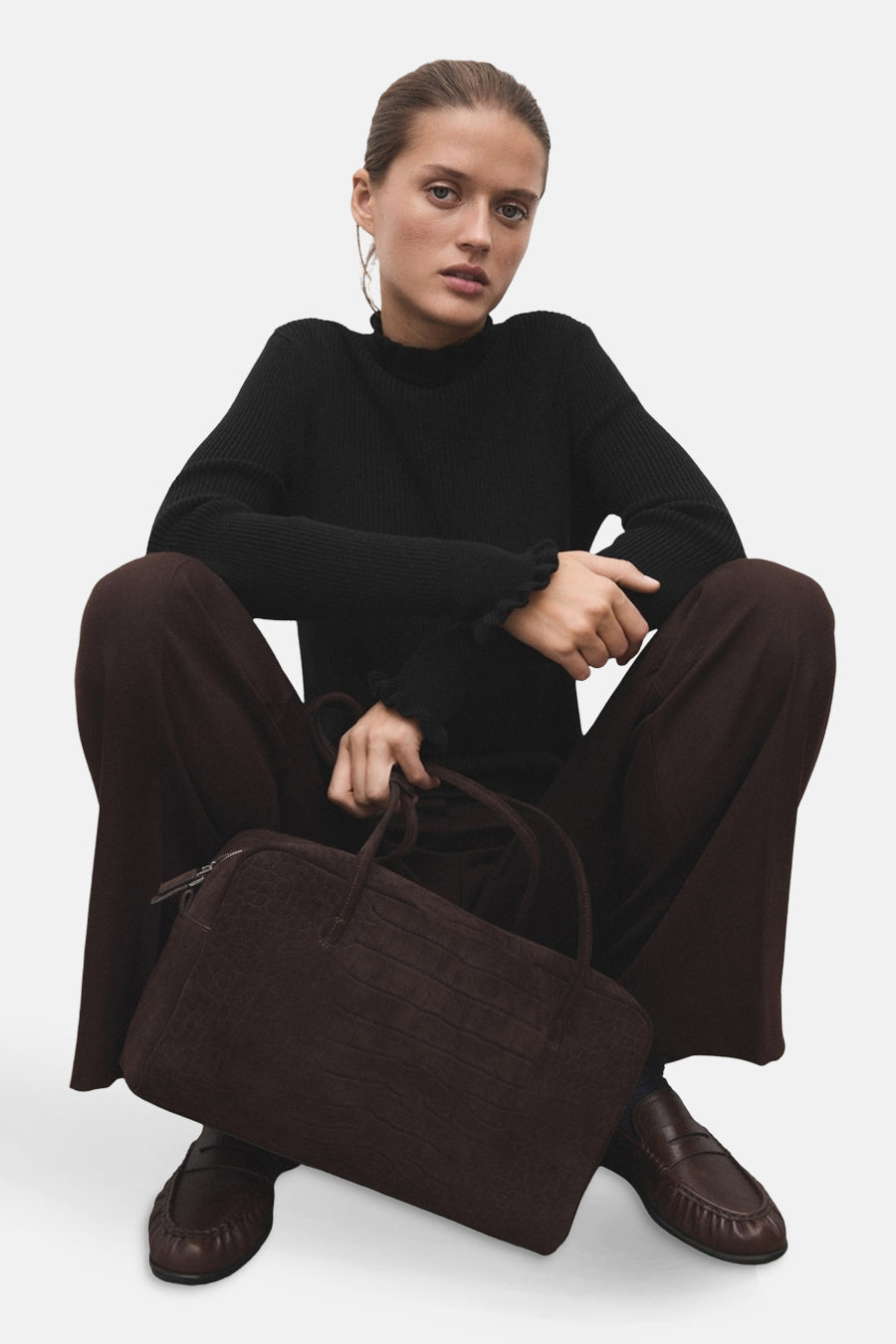 Zwarte rondehals trui van MANGO, gedragen met een wijde bruine broek en leren loafers.