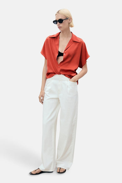 Oranje blouse met korte mouwen van MANGO, gedragen met een zwarte beha en een witte broek.