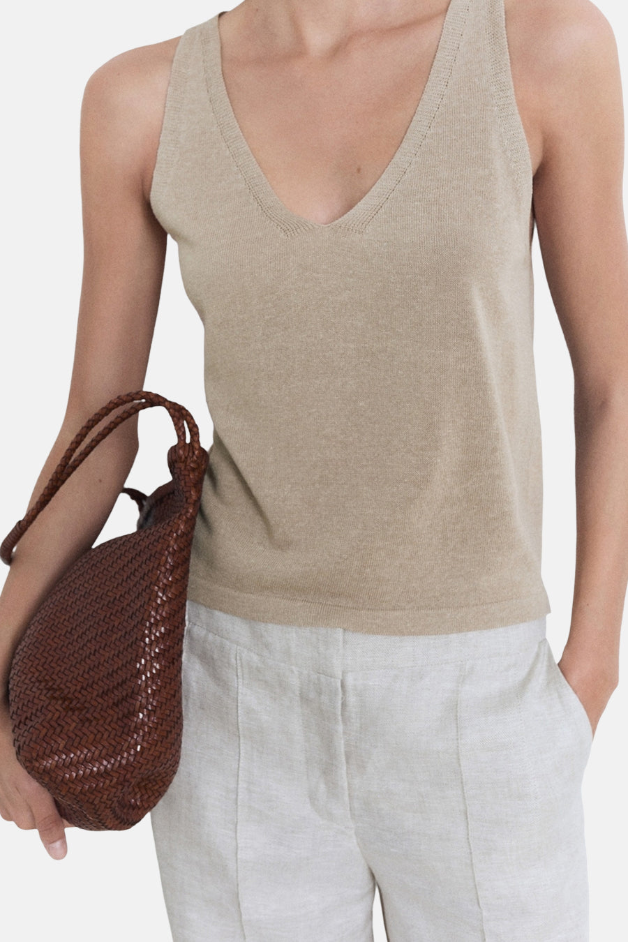 Beige tanktop van MANGO, gedragen met een lichtgekleurde linnen broek en een bruine gevlochten leren handtas.