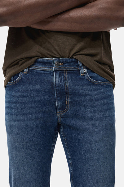 Jean slim bleu moyen de MANGO, porté avec un t-shirt marron, montrant les détails des poches et la texture du denim.