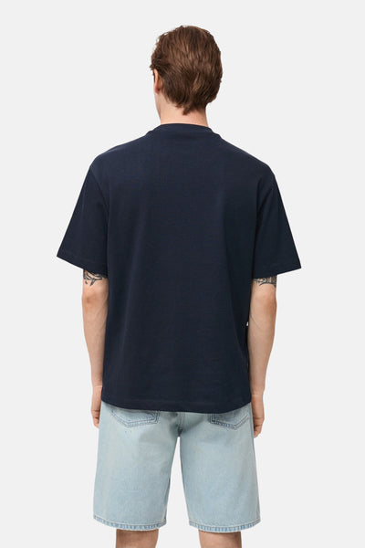 Donkerblauwe T-shirt met korte mouwen van MANGO, van achteren getoond, gedragen met een lichtblauwe spijkerbroek.