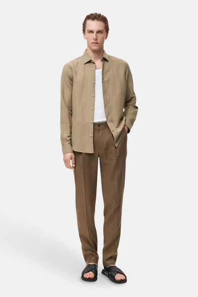 Kaki overhemd met lange mouwen van MANGO, open gedragen over een wit T-shirt, met een bruine broek en zwarte sandalen.