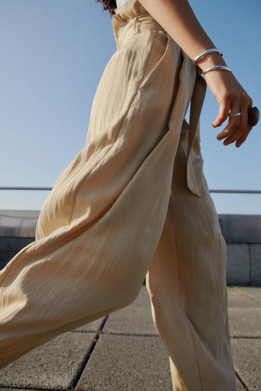 Beige broek van MANGO, wijd en vloeiend, met zilveren armbanden en een stenen ring.